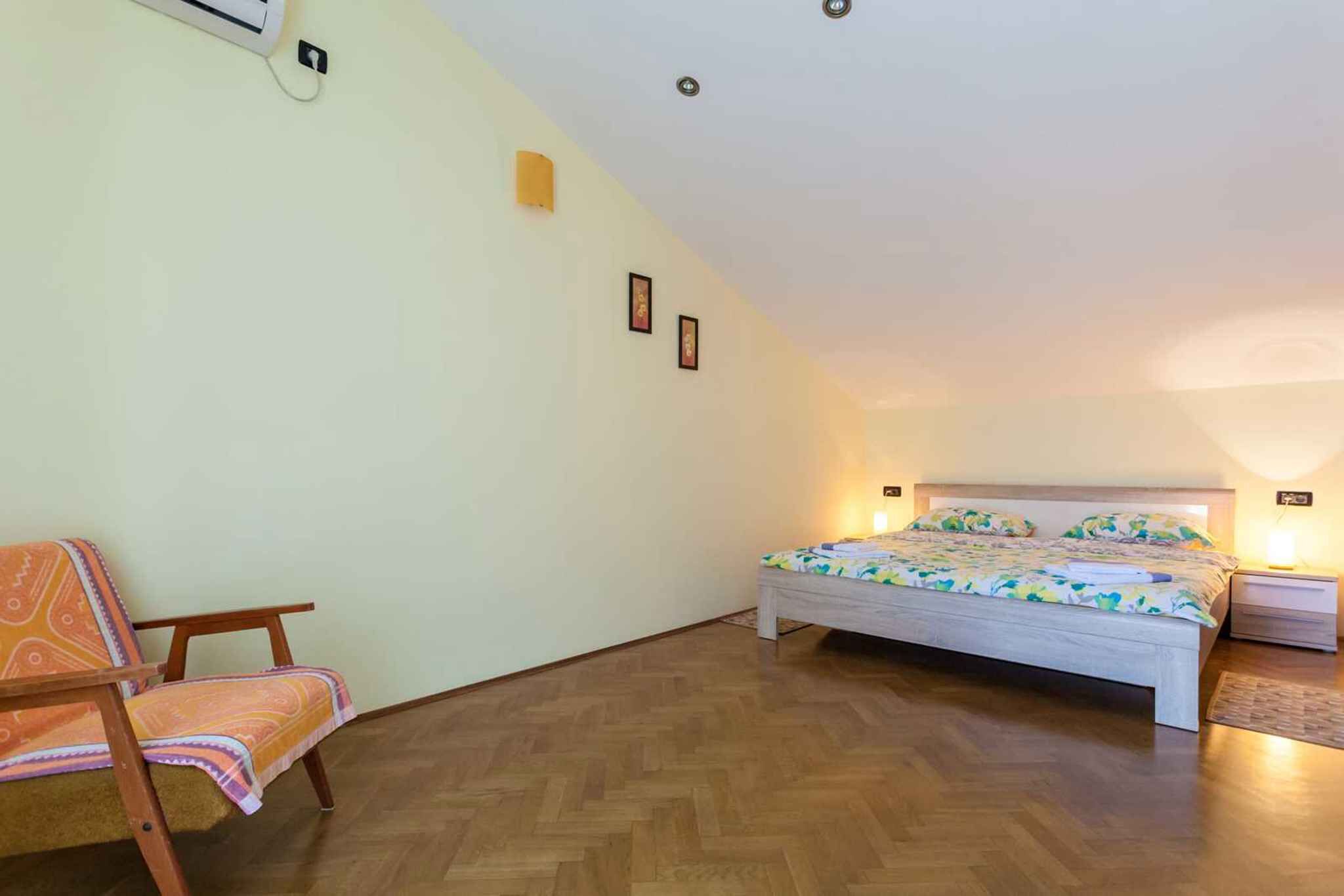 Un dormitorio con cama, una silla, una mesita de noche y aire acondicionado de pared.