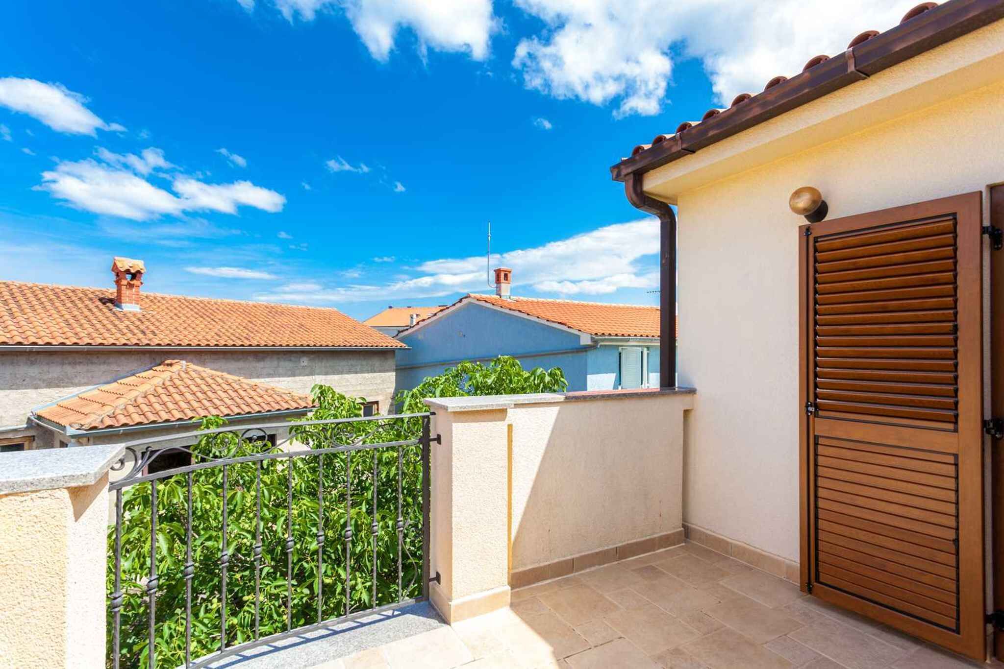 A balcony with a metal railing, a wooden door, and a tiled roof in the background.