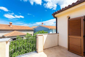 A balcony with a metal railing, a wooden door, and a tiled roof in the background. - Holiday apartment with two bedrooms and balcony (Porat)