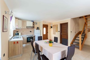A compact kitchen with modern appliances, a dining area with a table and chairs, and a wooden staircase.