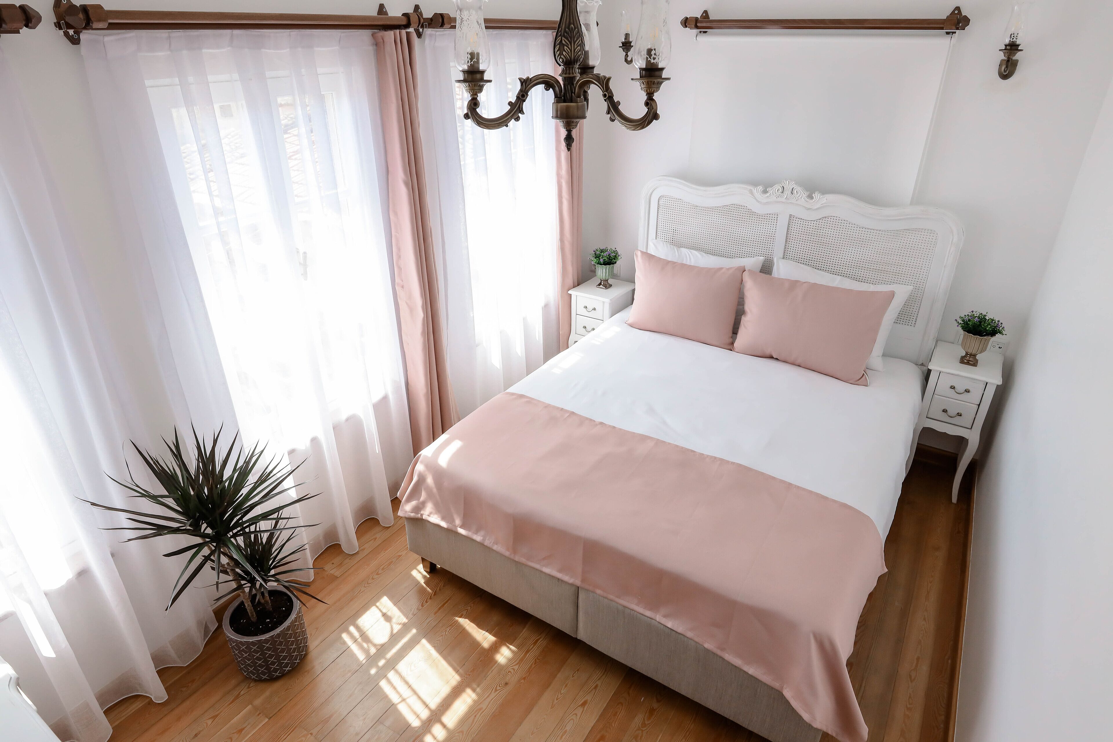 A bedroom with a bed, bedside tables, a potted plant, and a chandelier.
