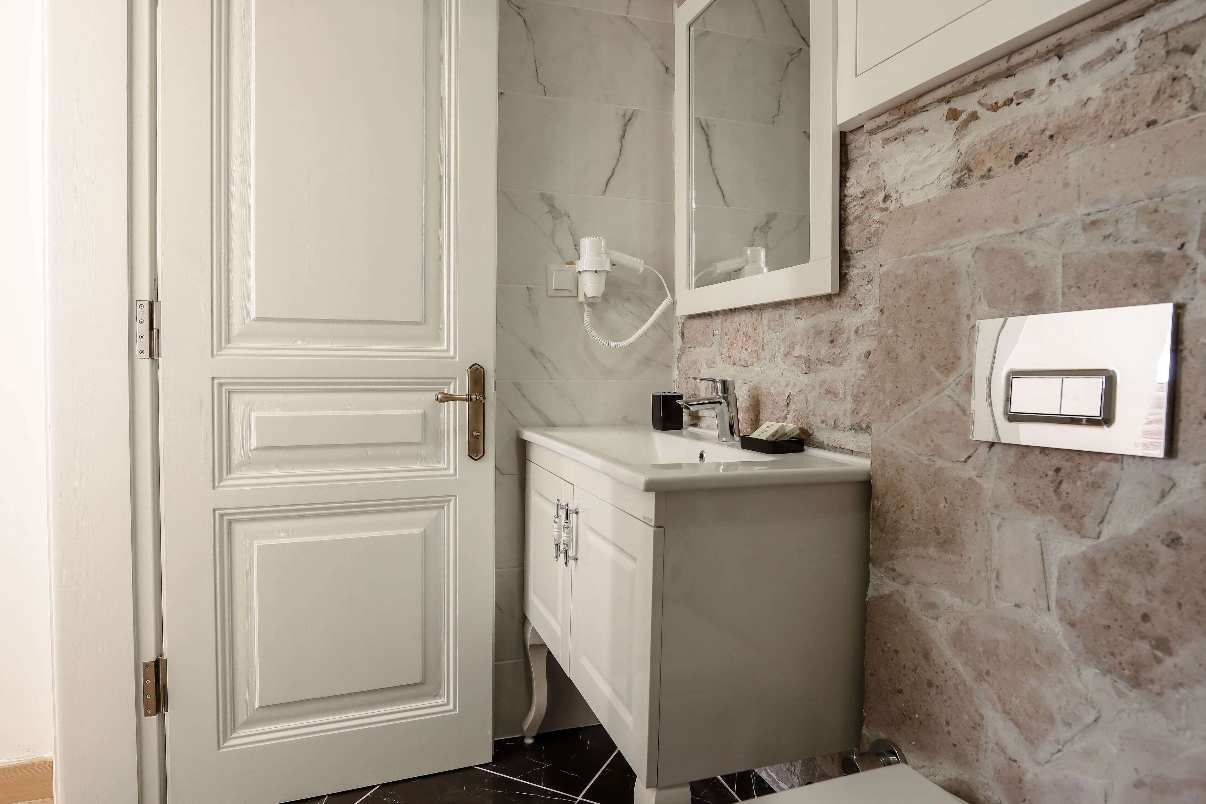 A bathroom with a white door, marble wall, and stone wall.
