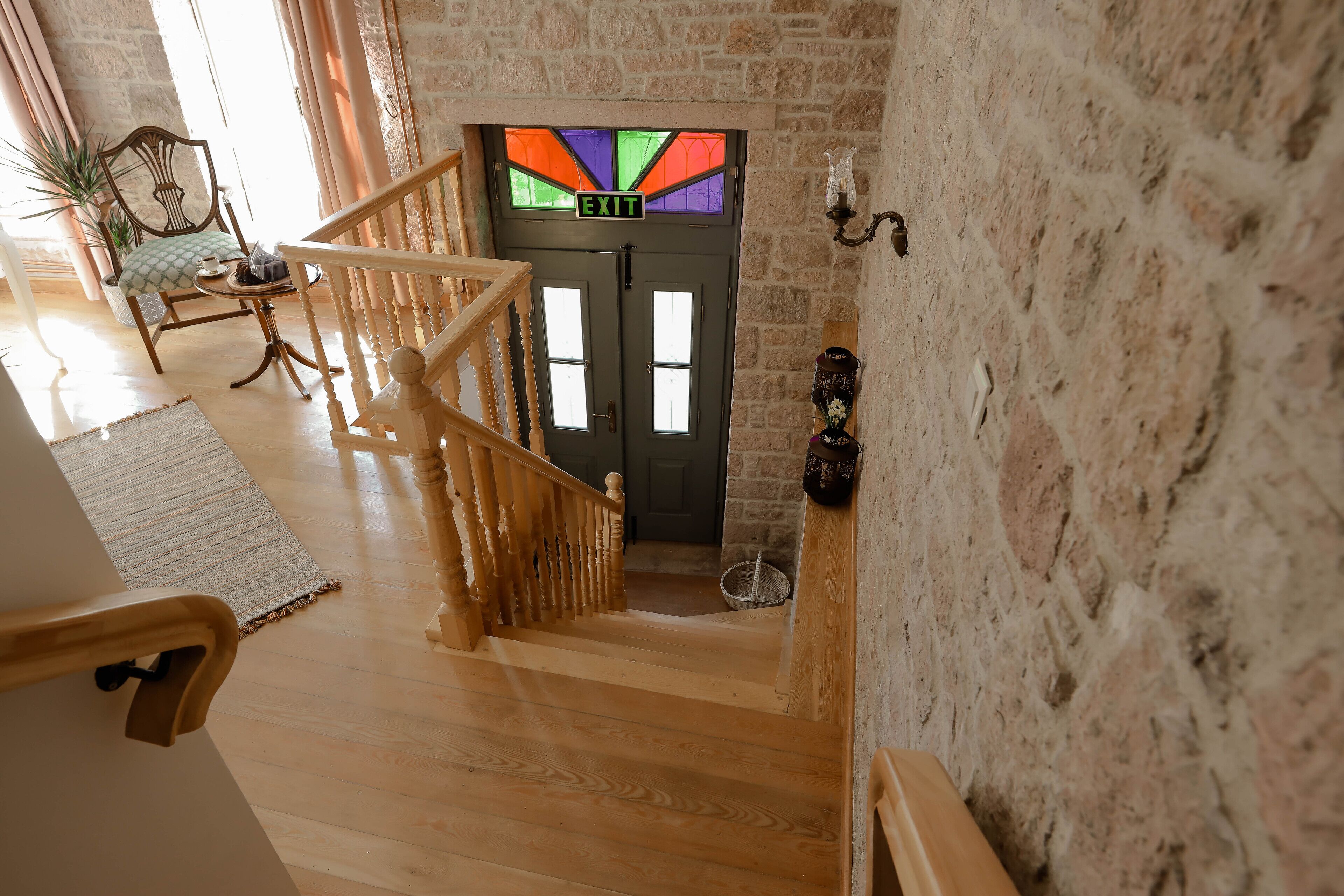 A wooden staircase leading to a door with an 'EXIT' sign, a potted plant, and a wall-mounted light fixture.