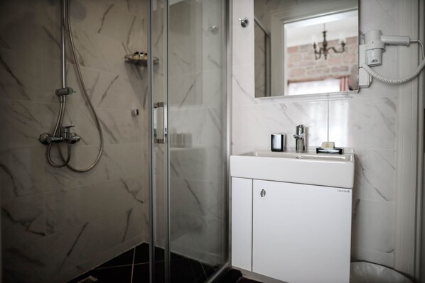 A modern bathroom with a glass-enclosed shower, a white sink with a mirror above, and a hairdryer mounted on the wall.