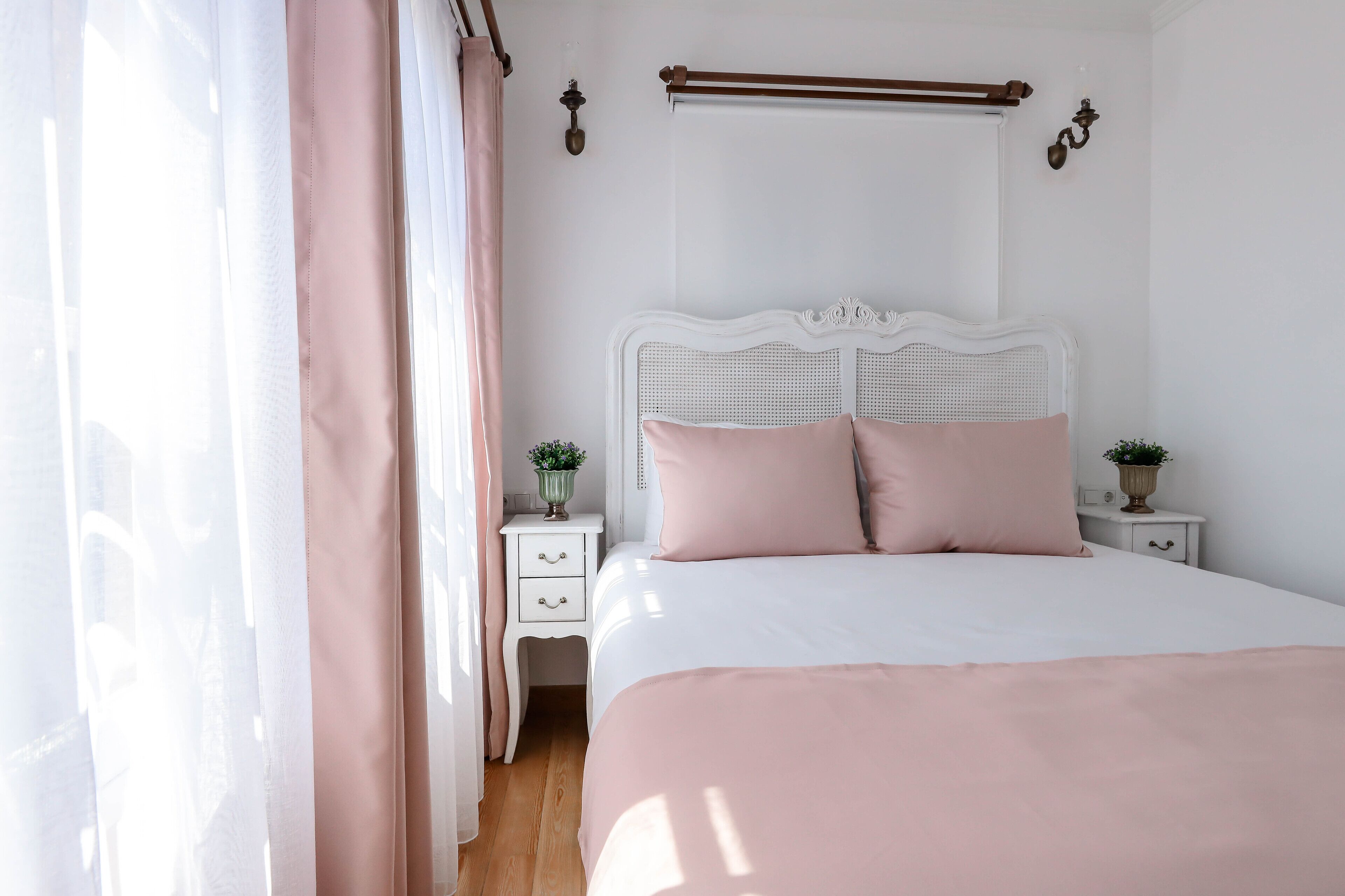 A bedroom with a white bed, two bedside tables, a white headboard, and a window with sheer curtains.