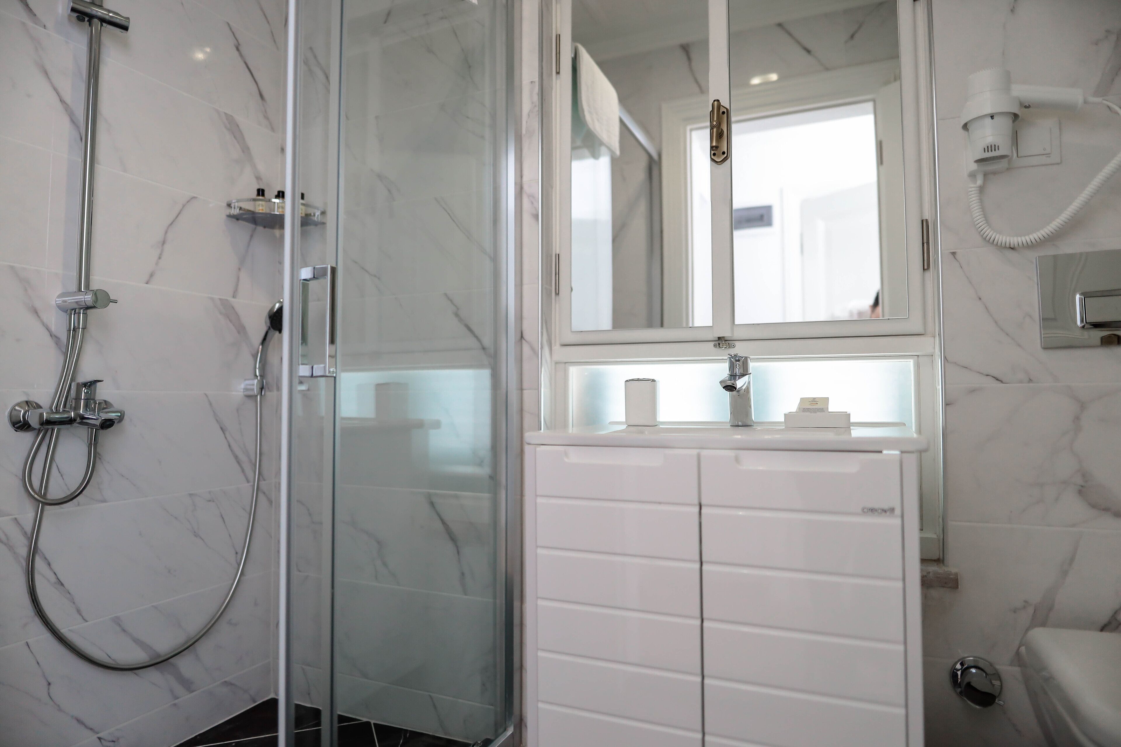 A bathroom with a glass-enclosed shower, a white sink with a mirror above it, and a toilet.