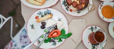 A table with plates of food including spring rolls, sausage, cheese, olives, and a cup of tea.