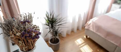 Un dormitorio con una cama, una mesita de noche con un jarrón de flores secas, una planta en maceta y un control remoto sobre la mesa.