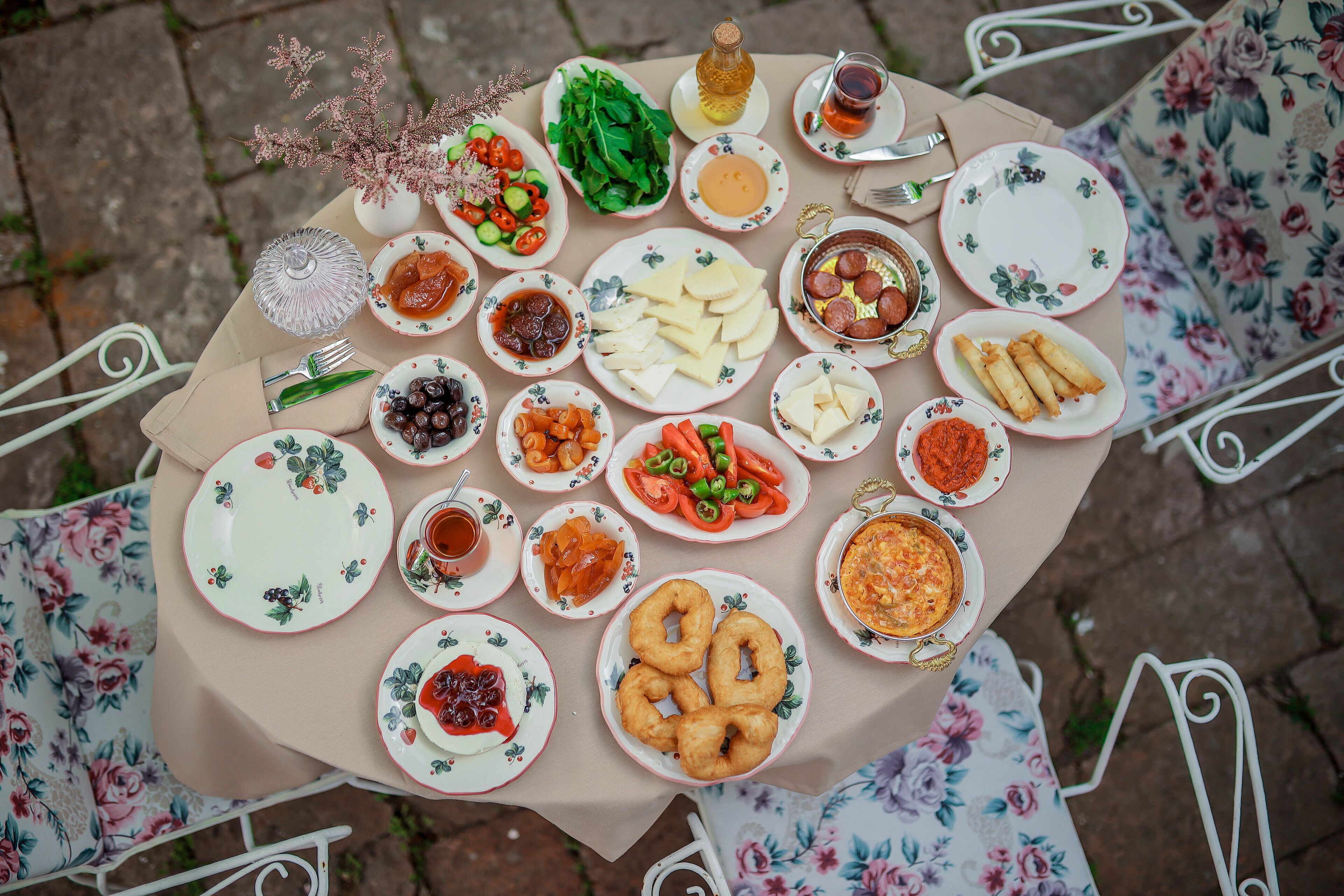 A table with various dishes and a bottle of olive oil, surrounded by floral chairs.