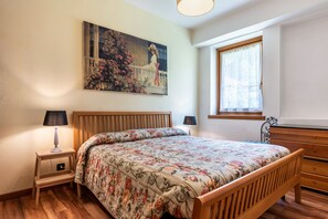 Une chambre avec un lit en bois, une table de chevet avec une lampe, une fenêtre avec des rideaux et un tableau accroché au mur.