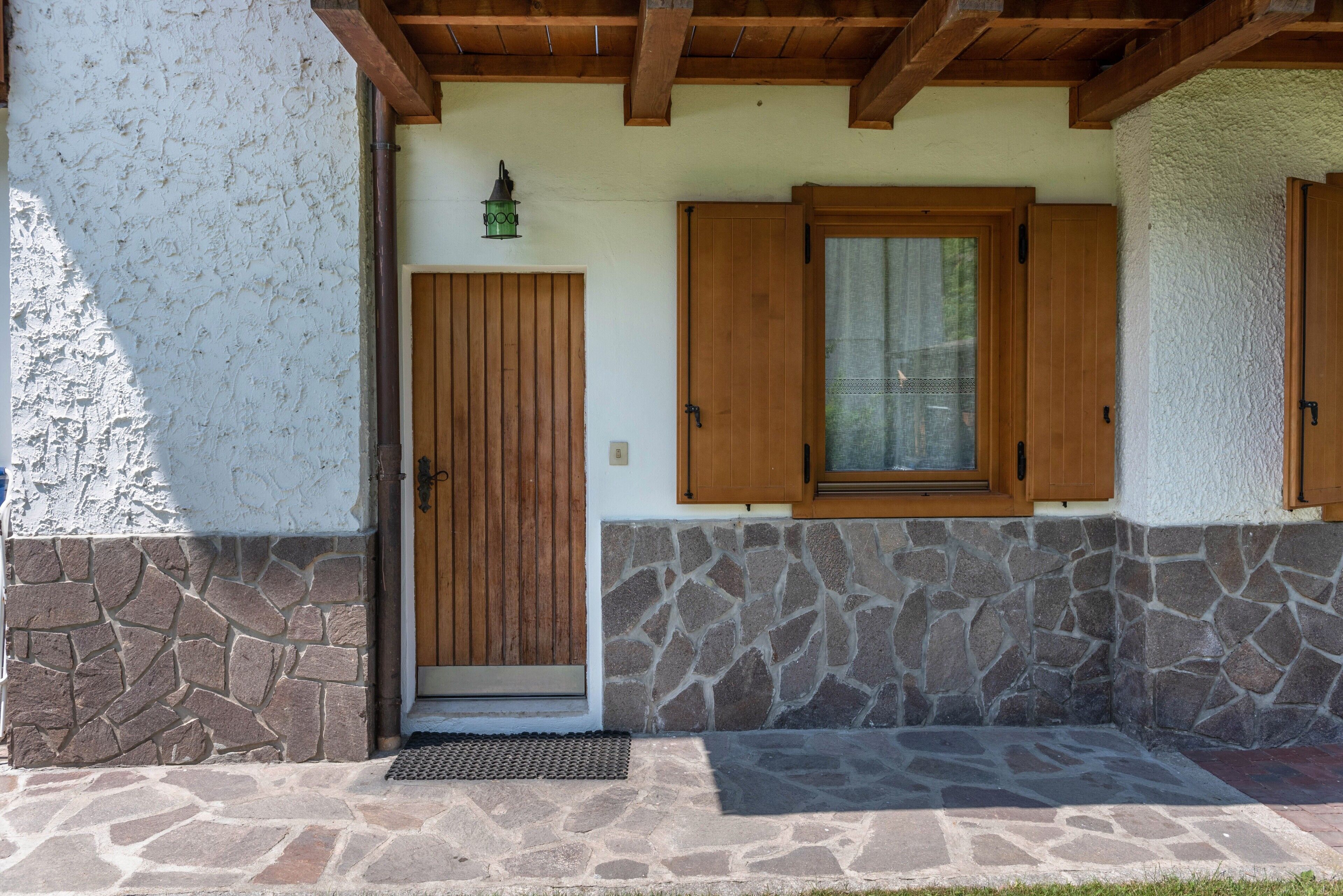 Eine Fassade aus Stein und Putz mit einer Holztür, einem Fenster mit Fensterläden und einem Steinsims.