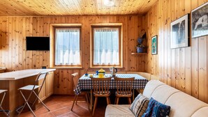 L’intérieur d’une cabane en bois comprend une table à manger, des chaises, un canapé et un téléviseur fixé au mur.
