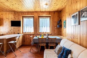 L’intérieur d’une cabane en bois comprend une table à manger, des chaises, un canapé et un téléviseur fixé au mur.