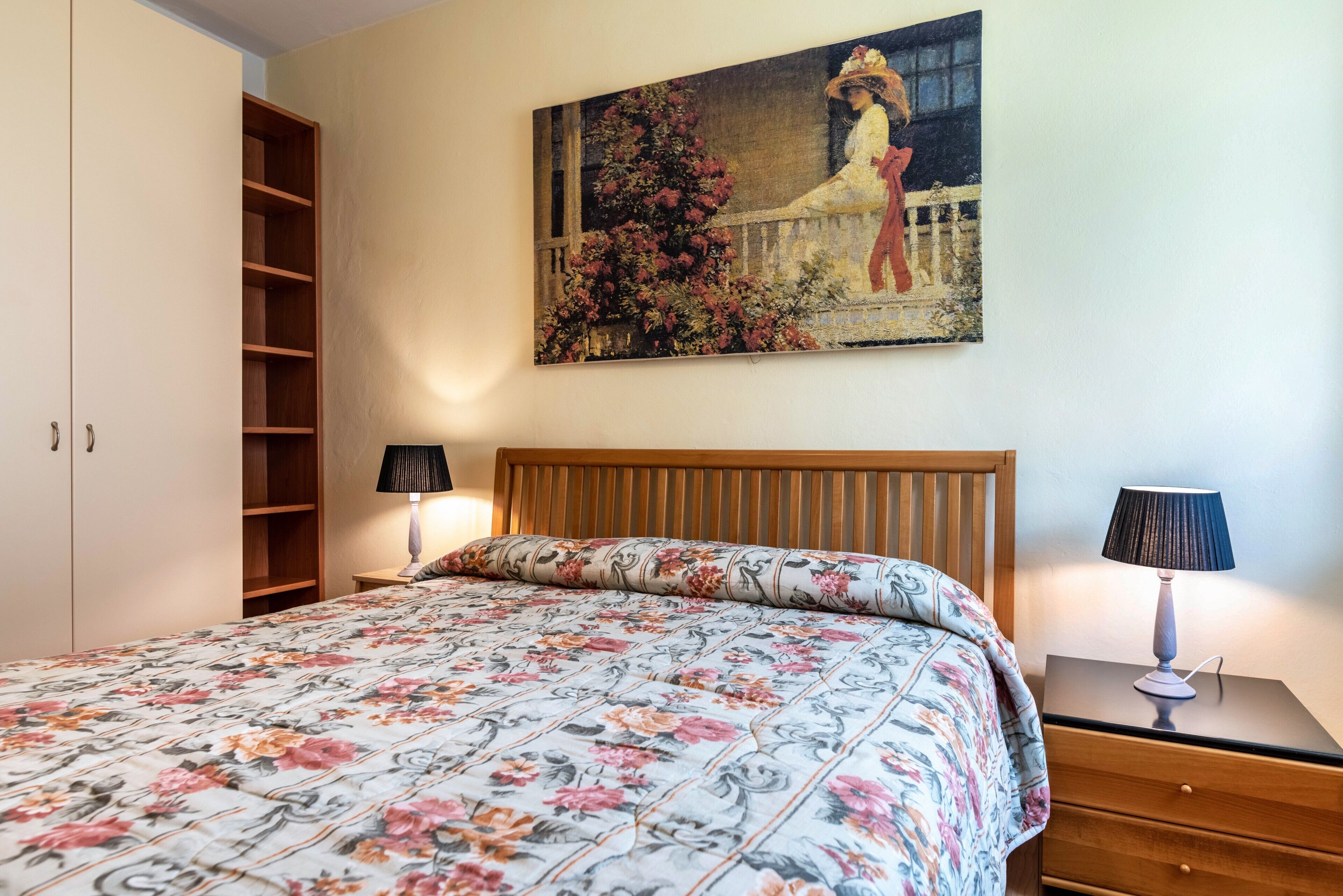 Une chambre à coucher avec un lit, une table de chevet, une lampe, une armoire et un tableau au mur.