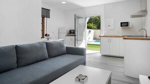 Un salon moderne avec un canapé gris, une table basse blanche et un coin cuisine doté de meubles blancs et d’un four à micro-ondes.