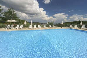 A swimming pool with lounge chairs and umbrellas, surrounded by a fence and greenery.