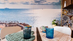 A table with two blue glass tumblers on green coasters, a white chair, and a view of the sea with a pier in the background. - Studio 'Mono Le Lecce 38B' with Pool and Balcony (Capoliveri)