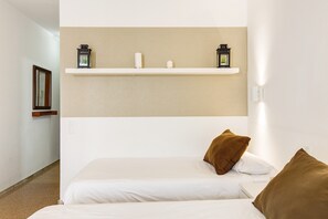A hotel room with a bed, two pillows, a shelf with decorative items, and a wall-mounted light fixture.