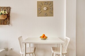 A white table with two chairs and a basket of oranges on it.
