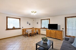 Ein Wohnzimmer mit Fernseher, einer Couch, einem Esstisch, Stühlen und einer Küchenzeile mit Schränken und einem Herd.