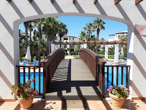 A wooden bridge leading to a swimming pool with palm trees and lounge chairs in the background. - Holiday Apartment 'Casita Dorada Cala d'Or' near Beach with Pool & Wi-Fi (Cala D'or)