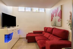 A modern living room with a red sectional sofa, a flat-screen TV, a white cabinet with blue lighting, and a painting of pink flowers on the wall. - Holiday Home Ca Martina Sonora Golf with Pool, Garden and Wi-Fi (Maspalomas)