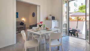 A dining area with a table, chairs, and a kitchen area with a microwave. - Apartment Casa Vacanza Soffio with Terrace, A/C & Wi-Fi (alghero)