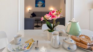 A dining table with a teapot, cups, a packet of coffee, a spoon, a vase with flowers, and pastries. - Apartment Casa Vacanza Soffio with Terrace, A/C & Wi-Fi (alghero)