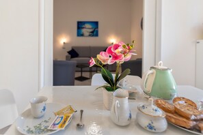 Une table à manger avec une théière, des tasses, un paquet de café, une cuillère, un vase de fleurs et des pâtisseries.
