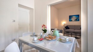 A dining area with a table set for two, a kettle, a vase with flowers, and a painting on the wall. - Apartment Casa Vacanza Soffio with Terrace, A/C & Wi-Fi (alghero)