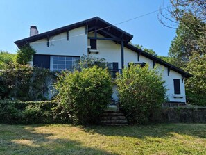 Una casa a due piani con un tetto spiovente, un camino e un piccolo portico d'ingresso con delle scale.