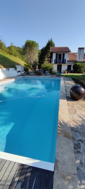 Una piscina rettangolare con acqua cristallina, circondata da un solarium in pietra e uno in legno.