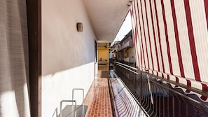 Un balcon étroit doté d’un sol carrelé, d’une rambarde en métal et offrant une vue sur les bâtiments adjacents.