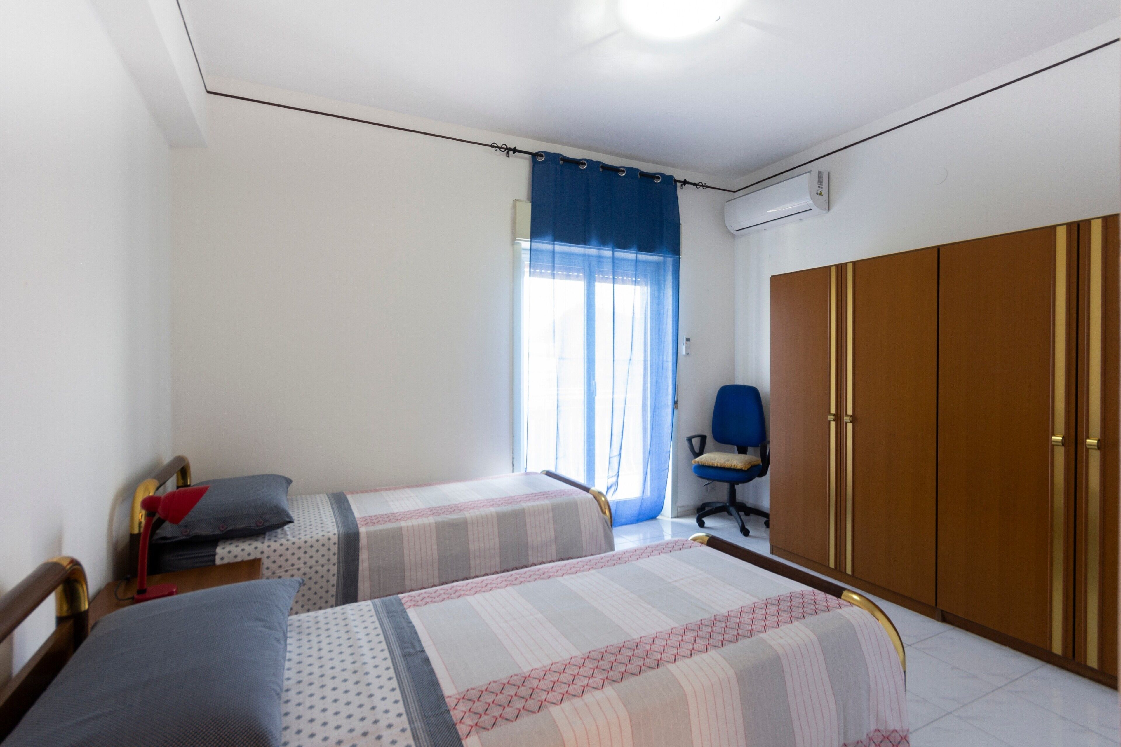 Une chambre avec deux lits, une chaise, une armoire et une fenêtre avec des rideaux.