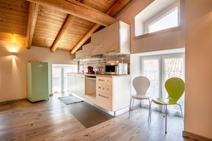 A modern kitchen with wooden beams, a green refrigerator, a microwave, and a white chair.