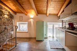 A kitchen with wooden beams, a green refrigerator, and a window with a white curtain.