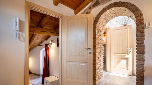 Une pièce avec un plafond en bois, une arche en briques, une porte blanche et un petit meuble blanc.
