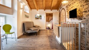 Une pièce avec un plafond en bois, un mur en pierre, un canapé, un fauteuil, un téléviseur fixé au mur et un escalier menant à un autre niveau.
