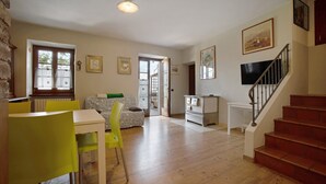 Un vaste espace de vie comprenant une table à manger, des chaises, un canapé, un escalier et un téléviseur fixé au mur.