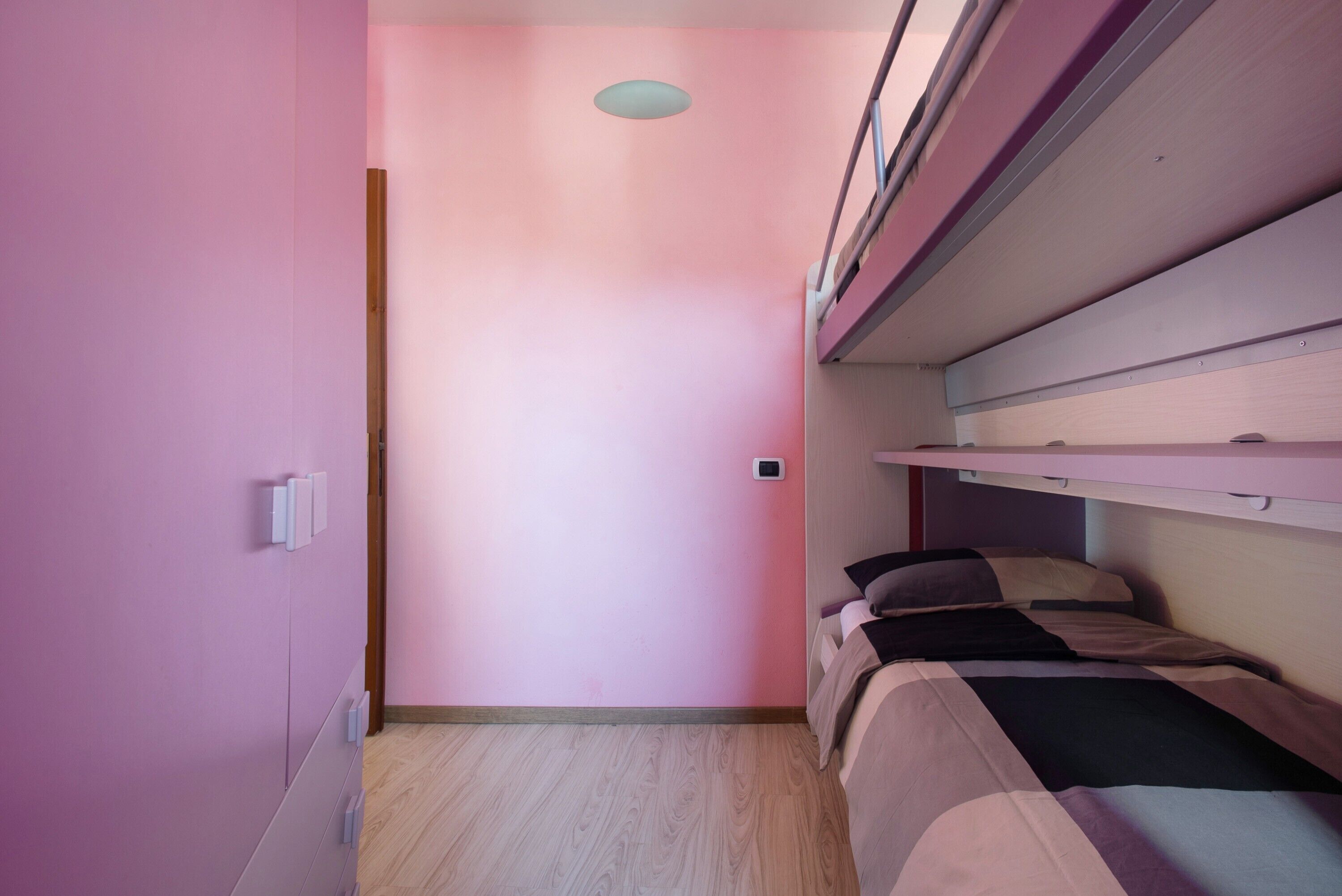 Ett rum med rosa väggar, en våningssäng, ett trägolv och en taklampa.