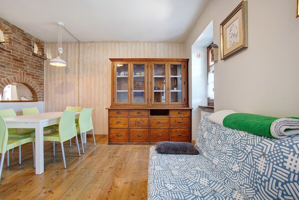 A room with a dining table, chairs, a cabinet, a sofa, and a patterned bedspread.