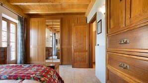 Une pièce aux murs lambrissés, comprenant un lit, une commode et une porte donnant sur une autre pièce.