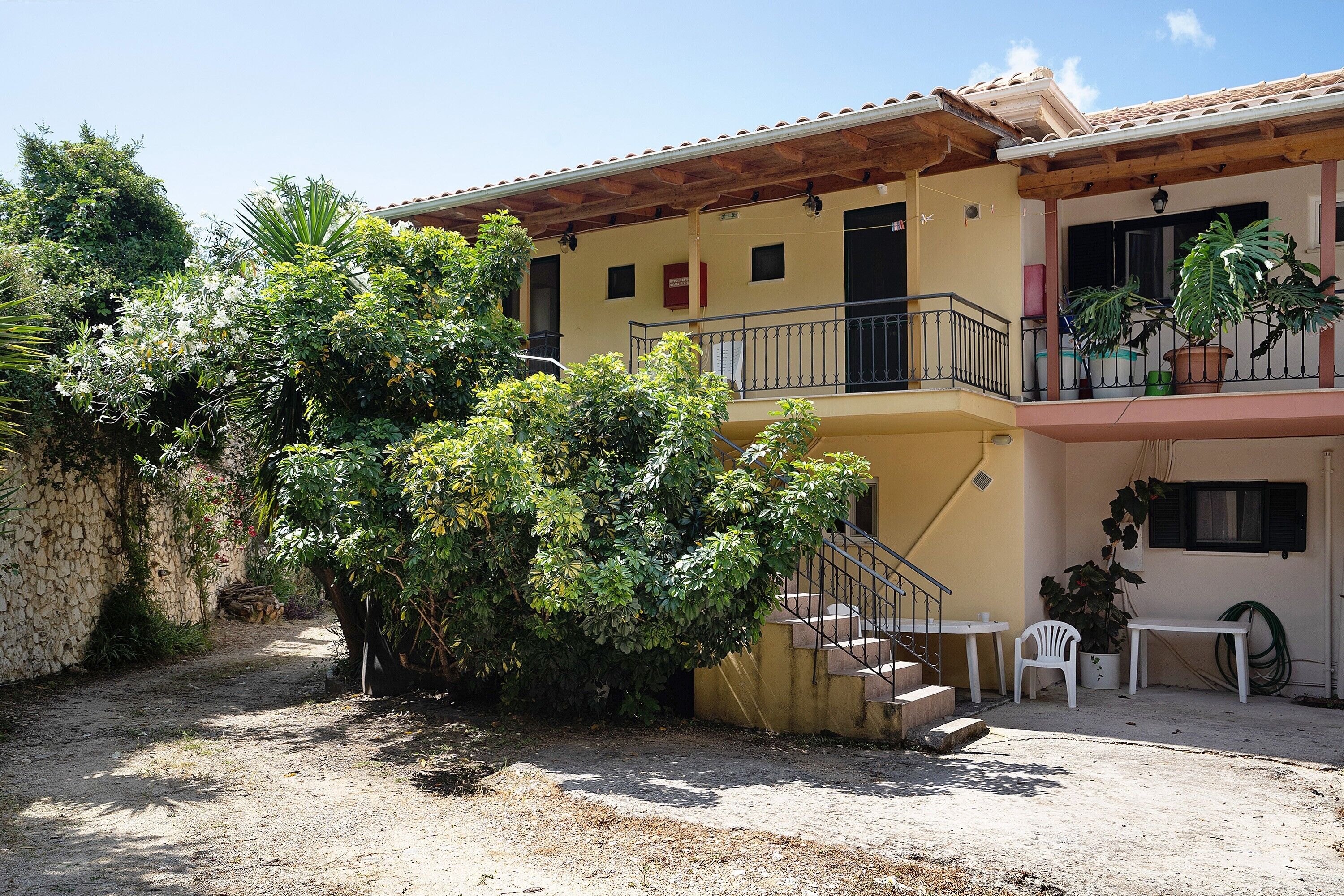 Un bâtiment à deux étages doté d’un balcon, d’un escalier et d’un petit patio avec une table et des chaises.