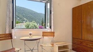 A room with a window, a wooden wardrobe, a table, and two chairs. - Vardia Studio B: Sea View, Balcony, and Wi-Fi Close to the Beach (?e???da)