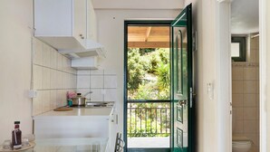A kitchen with a glass table, a stove, and a view of a garden through an open door. - Vardia Studio A Holiday Apartment with Sea View, Wi-Fi & Balcony (?e???da)
