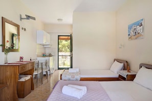 A hotel room with a wooden desk, a bed with a rolled towel, a painting on the wall, and a view through an open door.
