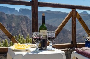 A table with a bottle of wine and two glasses, set against a mountainous backdrop. - Vacation Home "Silence Cave Rural House" with Moutain View, Terrace & Wi-Fi (Artenara)