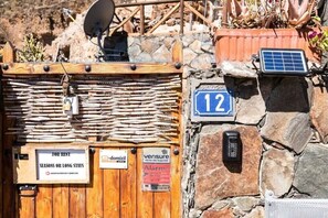 Ein rustikales Holztor mit Vermietungsschild, eine Steinsäule mit Hausnummer und eine Solarpanel-Anlage.
