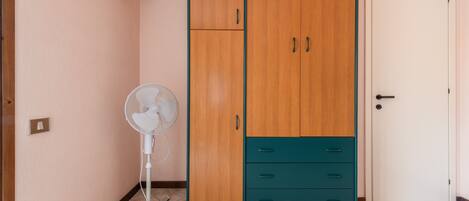 A room with a wardrobe, a fan, a door, and a tiled floor.