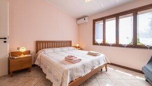 Un dormitorio con cama de madera, mesitas de noche con lámparas, una ventana con persianas y un equipo de aire acondicionado.